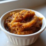 Close-up of rich, orange-brown homemade applesauce topped with cinnamon, served in a small white ramekin.