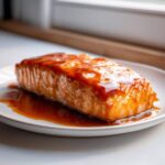 A perfectly cooked fillet of salmon covered in a thick, glossy honey garlic glaze, resting on a white plate.