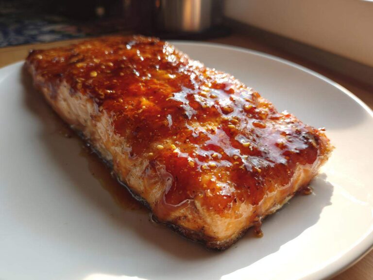 A perfectly cooked fillet of salmon coated in a thick, shiny honey garlic glaze, resting on a white plate.