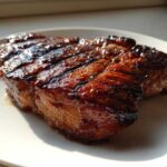 Close-up of a thick, juicy pork steak recipe cut, covered in a dark, shiny glaze, resting on a white plate.
