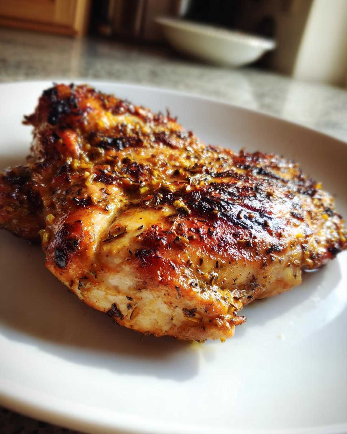 Close-up of a perfectly cooked, juicy greek chicken breast with a golden-brown, herbed crust on a white plate.