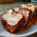 Close-up of thick, juicy slices of pork loin roast with a caramelized, seasoned exterior resting in pan juices.