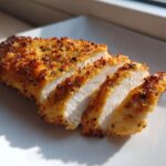 Close-up of a perfectly cooked, sliced air fryer chicken breast showing juicy white meat and a crispy, seasoned golden crust.