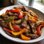 Close-up of sizzling steak fajitas featuring strips of seasoned beef mixed with colorful bell peppers and onions in a white bowl.