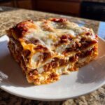 A thick, square slice of baked lasagna with visible layers of meat sauce and cottage cheese, topped with melted mozzarella.
