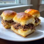 Three delicious mississippi pot roast sliders piled high with shredded beef on shiny, toasted slider buns.