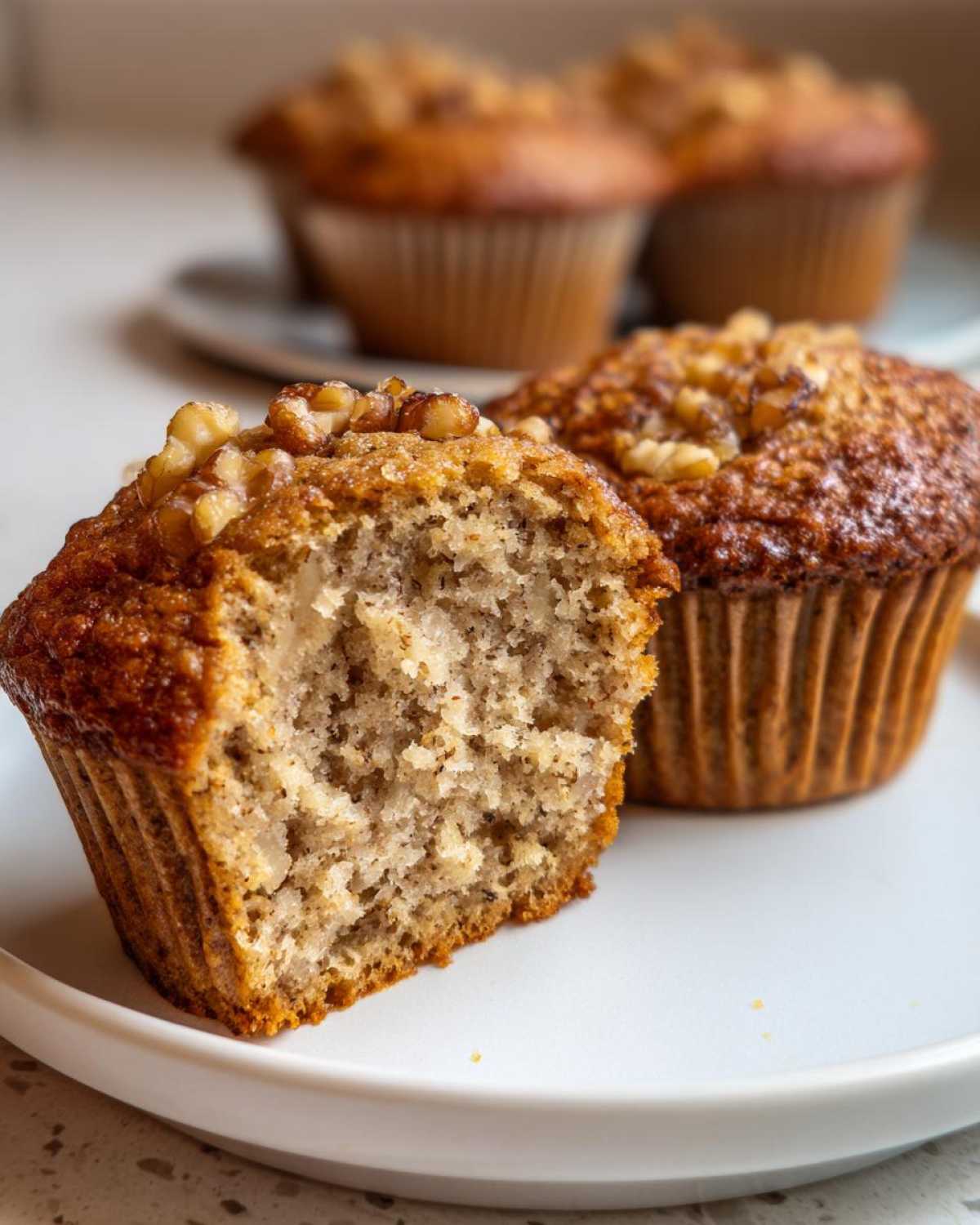 Close-up of a moist banana nut muffin cut in half showing the crumb texture and walnuts on top.