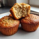 Close-up of three golden brown banana protein muffins stacked on a plate, one cut open showing the moist interior.