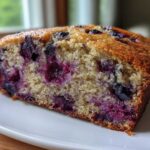 Close-up of a moist slice of blueberry banana bread showing a golden crust and vibrant purple blueberries throughout the crumb.