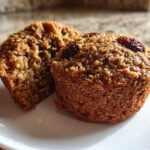 Close-up of two moist bran muffins, one cut open to show texture, topped with raisins.