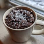 Close-up of a moist chocolate mug cake topped with chocolate chips and powdered sugar, ready to eat.