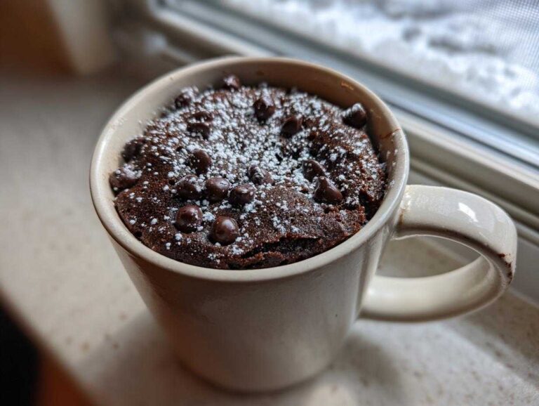 Moistest 75-second Chocolate mug cake Craving Solved Close-up of a moist chocolate mug cake topped with chocolate chips and powdered sugar, ready to eat.