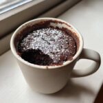 Close-up of a moist chocolate mug cake dusted with powdered sugar, ready to eat.