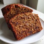 Close-up of two thick slices of moist date nut bread showing rich brown color, dates, and chopped nuts.