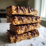 Four stacked, no-bake protein bars made with oats and drizzled generously with melted dark chocolate.