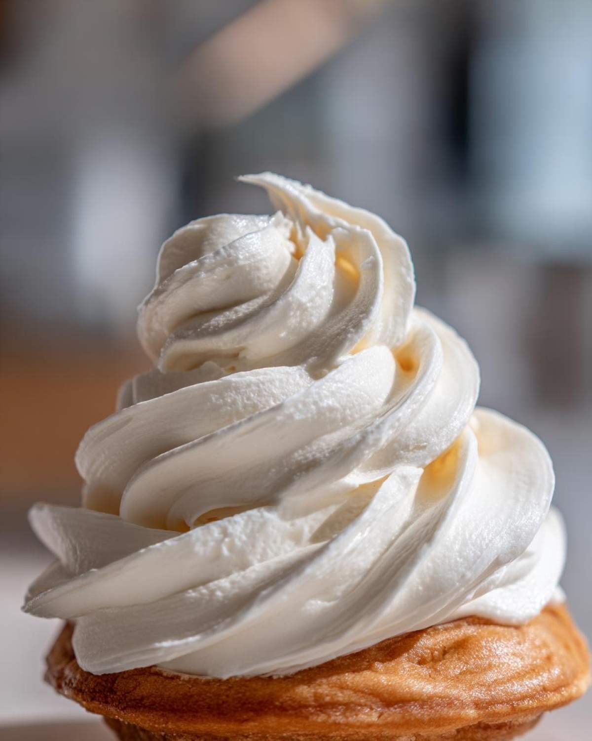 Close-up of a perfectly piped swirl of fluffy cream cheese frosting atop a golden cupcake base.