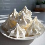 A pile of crisp, white, perfectly piped meringue cookies displayed on a small white plate.
