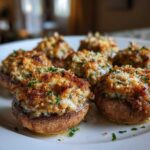 Close-up of several golden brown Sausage stuffed mushrooms with crispy breadcrumb topping on a white plate.