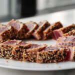 Slices of perfectly Seared Ahi Tuna, crusted with black and white sesame seeds, arranged on a white plate.