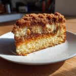 A close-up slice of moist coffee cake featuring a thick brown sugar crumb topping and a visible cream cheese swirl layer.