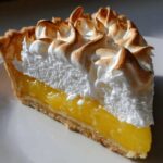 Close-up of a slice of lemon meringue pie showing bright yellow filling and toasted meringue peaks.