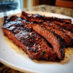 Close-up of medium-rare sliced steak glistening with a rich Carne asada marinade glaze on a white plate.