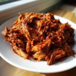 Close-up of perfectly shredded Slow Cooker Pulled Pork coated in rich BBQ sauce, served on a white plate.