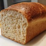 Close-up of a freshly baked loaf of whole wheat bread, showing a golden-brown crust and a soft, light crumb texture.