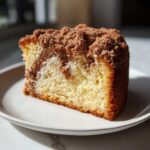 A close-up of a moist slice of sour cream coffee cake featuring a cinnamon swirl and thick, crumbly streusel topping.