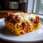A thick, square slice of baked spaghetti pie layered with meat sauce and topped with gooey melted mozzarella cheese.