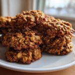 A close-up stack of golden brown, textured breakfast cookie made with visible oats, sitting on a white plate.