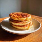 A tall stack of golden brown sourdough pancakes drizzled with syrup on a white plate.