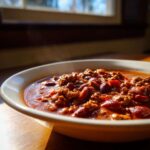 Close-up of a steaming bowl of rich, hearty crockpot chili filled with ground beef and kidney beans.