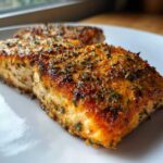 Close-up of a golden-brown, seasoned fillet of air fryer salmon resting on a white plate.