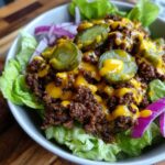 Close-up of a delicious cheeseburger bowl with seasoned ground beef, melted cheese sauce, pickle slices, and red onion on lettuce.