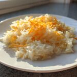 A serving of fluffy white rice topped with shredded orange cheddar cheese, making delicious cheesy rice.