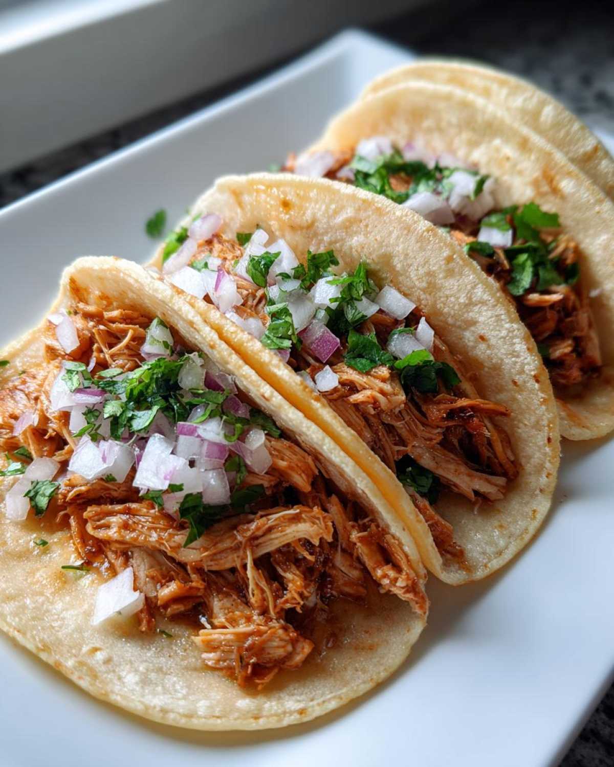 Three soft corn tortillas filled with shredded seasoned chicken, topped with diced white onion and fresh cilantro for amazing chicken tacos.