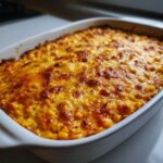 Close-up of a baked, creamy corn dip with a bubbly, browned cheese topping in a white casserole dish.