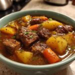 Close-up of a hearty bowl of amazing pork stew featuring tender meat chunks, golden potatoes, and bright carrots in a rich broth.