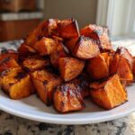A pile of beautifully caramelized and slightly charred roasted sweet potato cubes on a white plate.