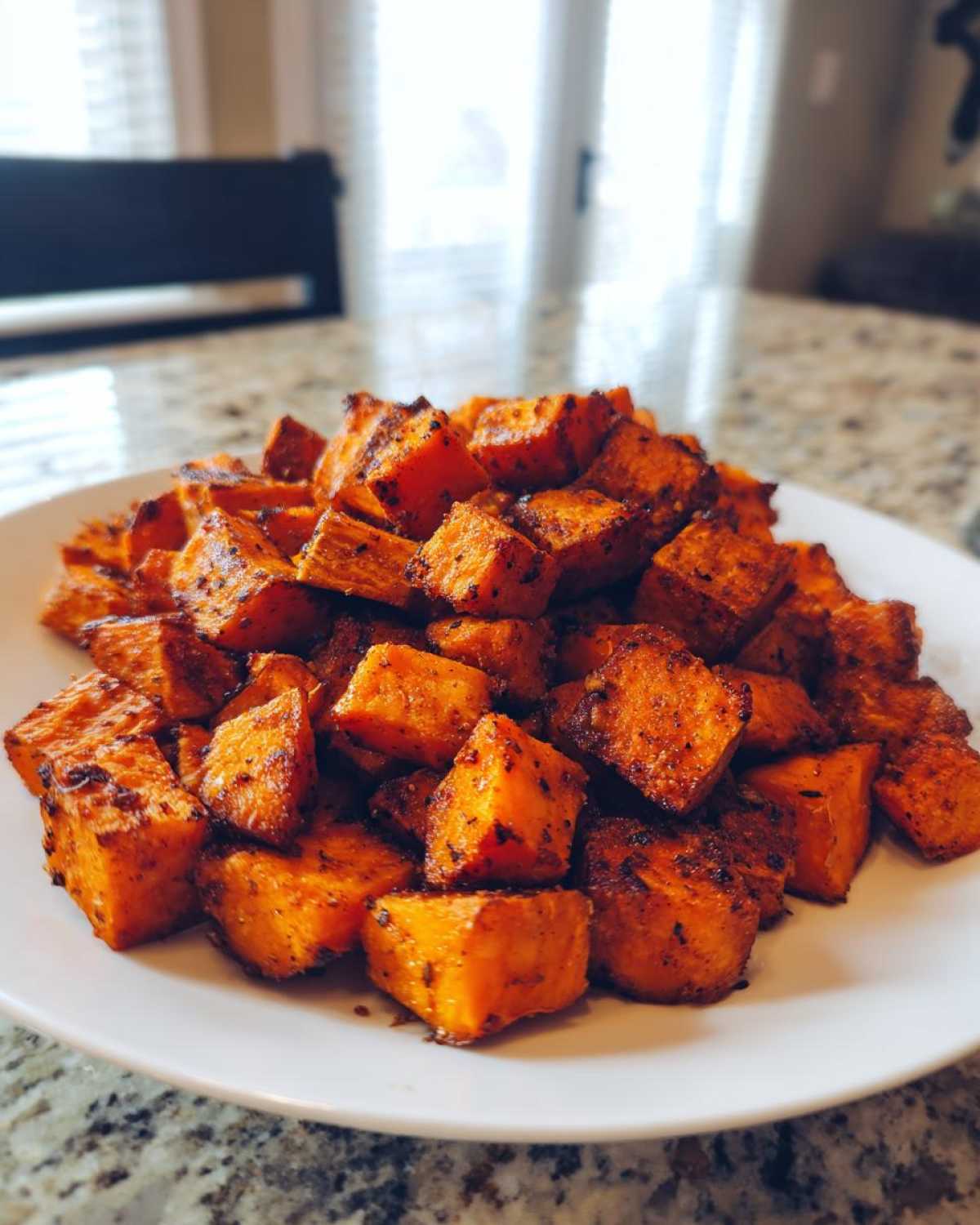 A white plate piled high with perfectly seasoned, caramelized roasted sweet potato cubes.