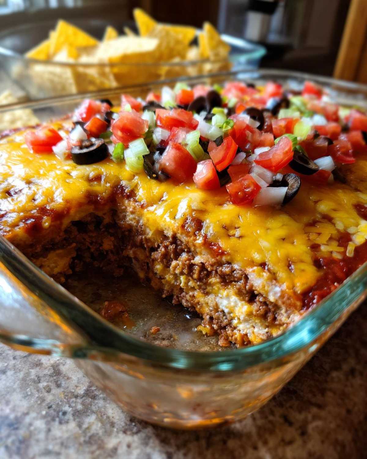 A close-up view of the amazing Seven layer dip in a glass dish, showing layers of meat, cheese, and toppings like tomatoes and olives.