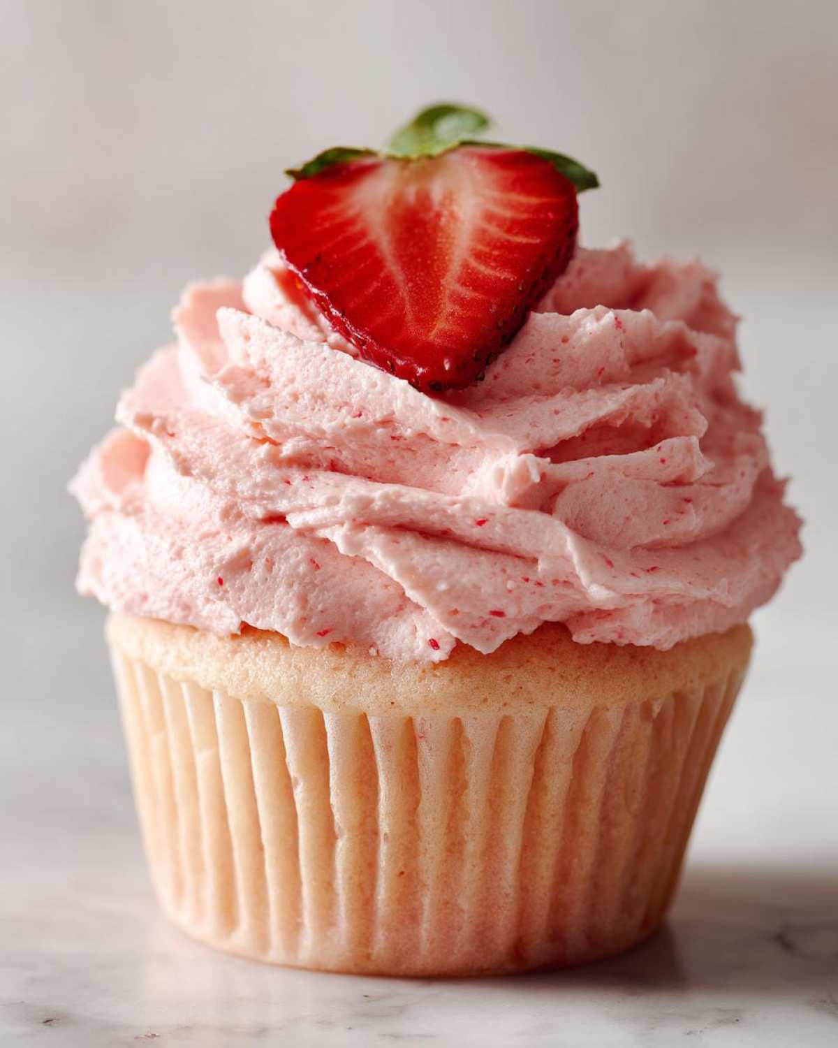 A single, beautifully frosted cupcake topped with pink strawberry frosting and a fresh strawberry slice, showcasing amazing strawberry cupcakes.