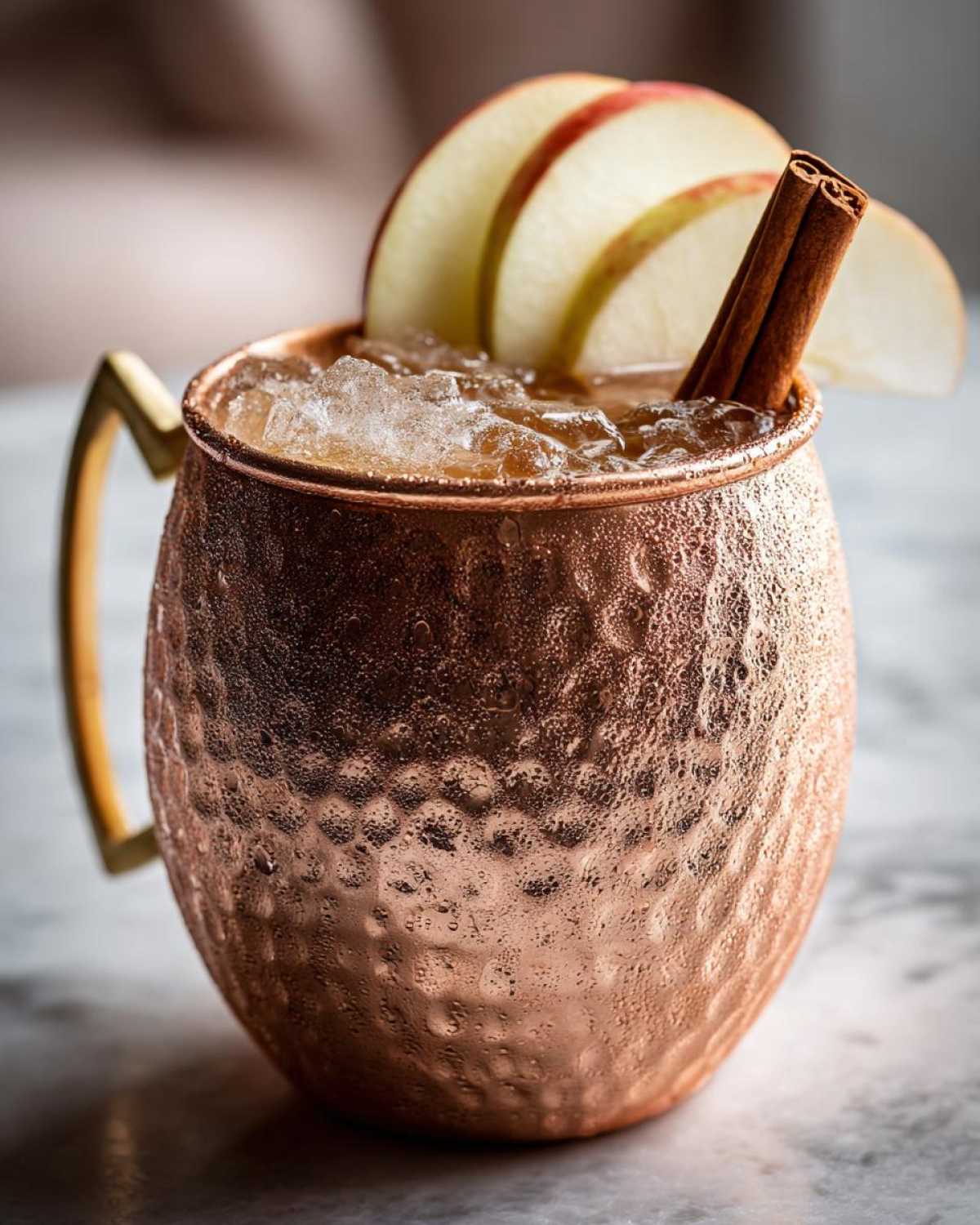 A close-up of a frosty copper mug filled with an apple cider moscow mule, garnished with apple slices and a cinnamon stick.