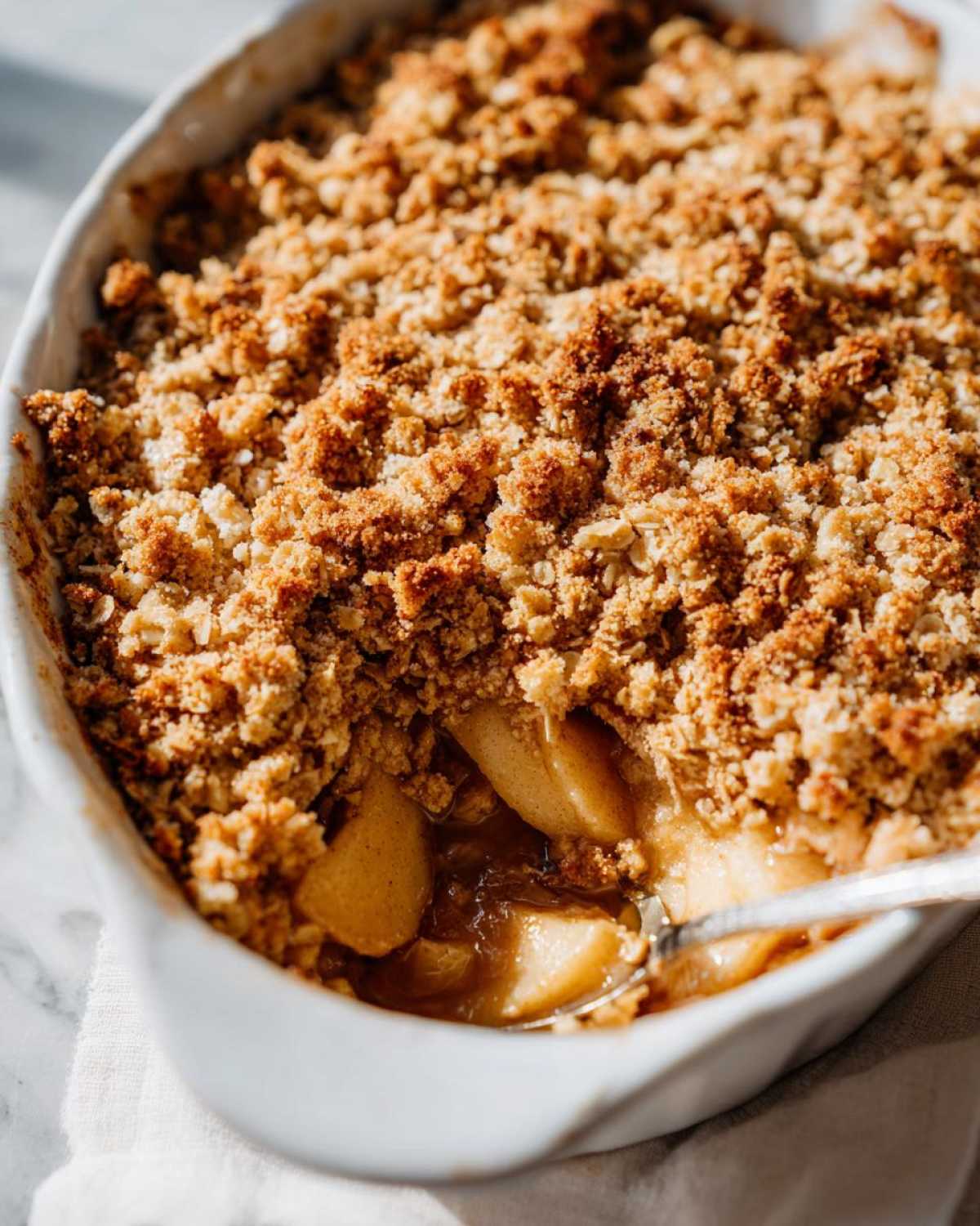 Close-up of a golden brown baked apple crisp recipe with a spoonful revealing soft, caramelized apple filling.