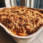 Close-up of a golden brown, crunchy topping on a freshly baked apple crisp recipe in a white baking dish.