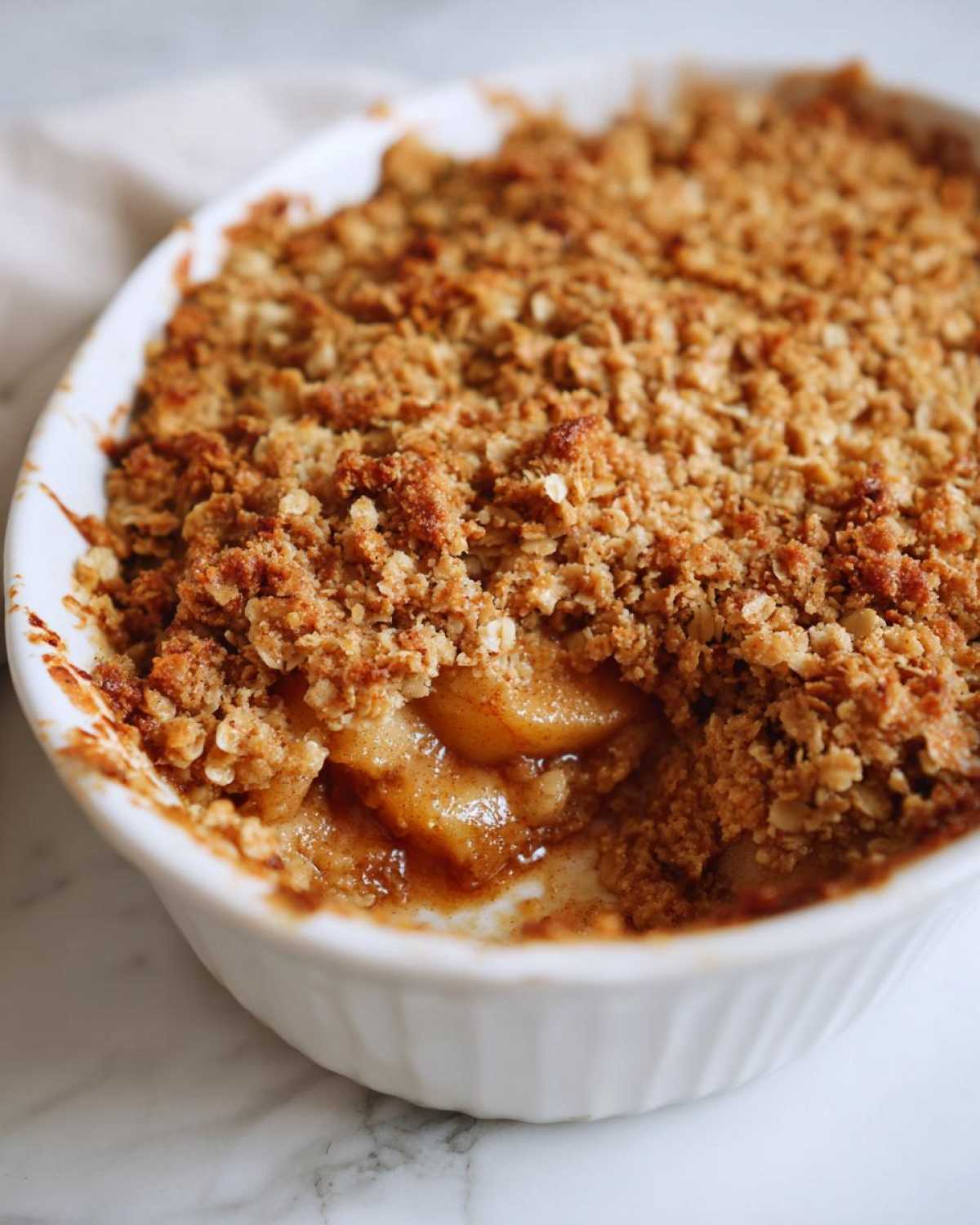 Close-up of a freshly baked apple crisp recipe in a white dish, showing bubbling cinnamon apples under a crunchy oat topping.