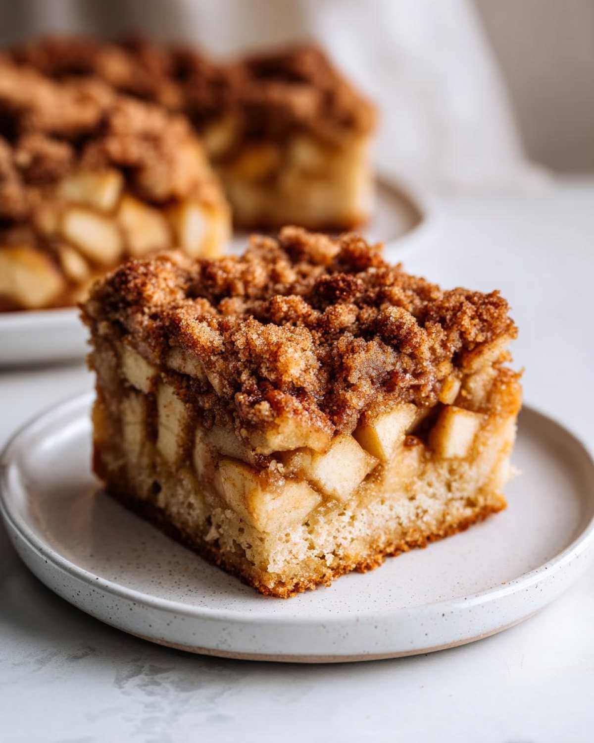 Close-up of a moist slice of apple crumb cake showing chunks of apple and a thick cinnamon streusel topping.