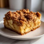 A close-up of a moist slice of apple crumb cake showing thick apple filling and a generous cinnamon streusel topping.