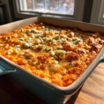 Close-up of hot, baked Buffalo chicken dip topped with melted cheese and blue cheese crumbles in a light blue baking dish.